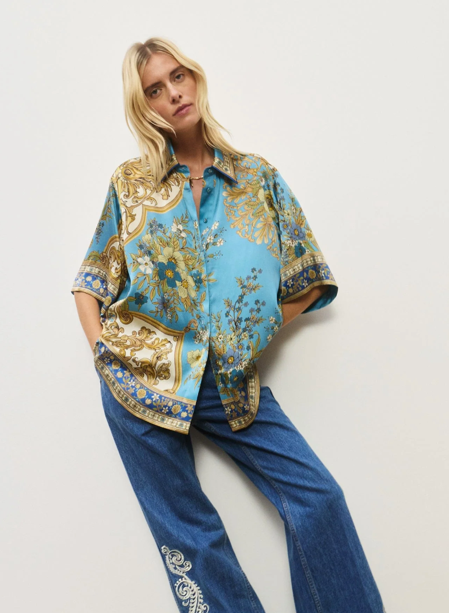 Woman wearing a patterned shirt and jeans on a white background
