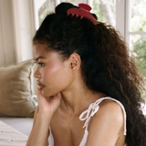Woman with a ponytail wearing a white top, sitting indoors.