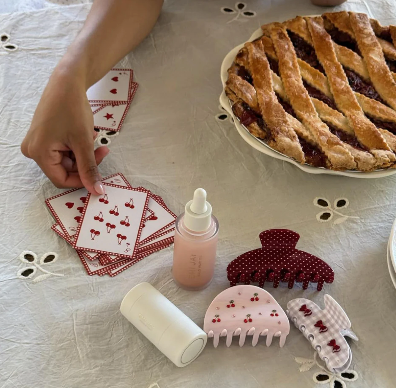 Table with playing cards, a pie, a bottle, and hair accessories on a floral tablecloth.