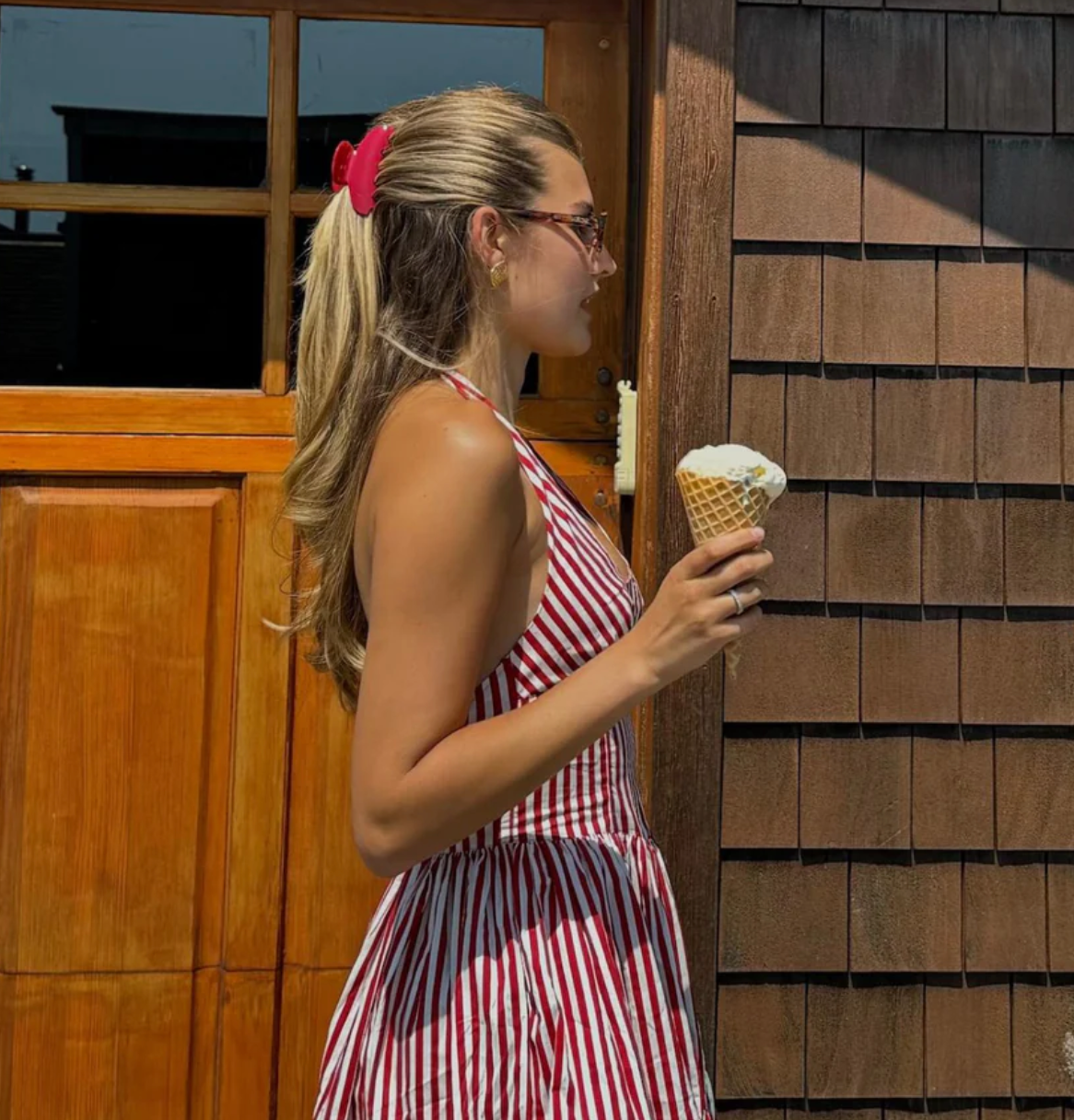 Woman in a red and white striped dress holding an ice cream cone in front of a wooden building.