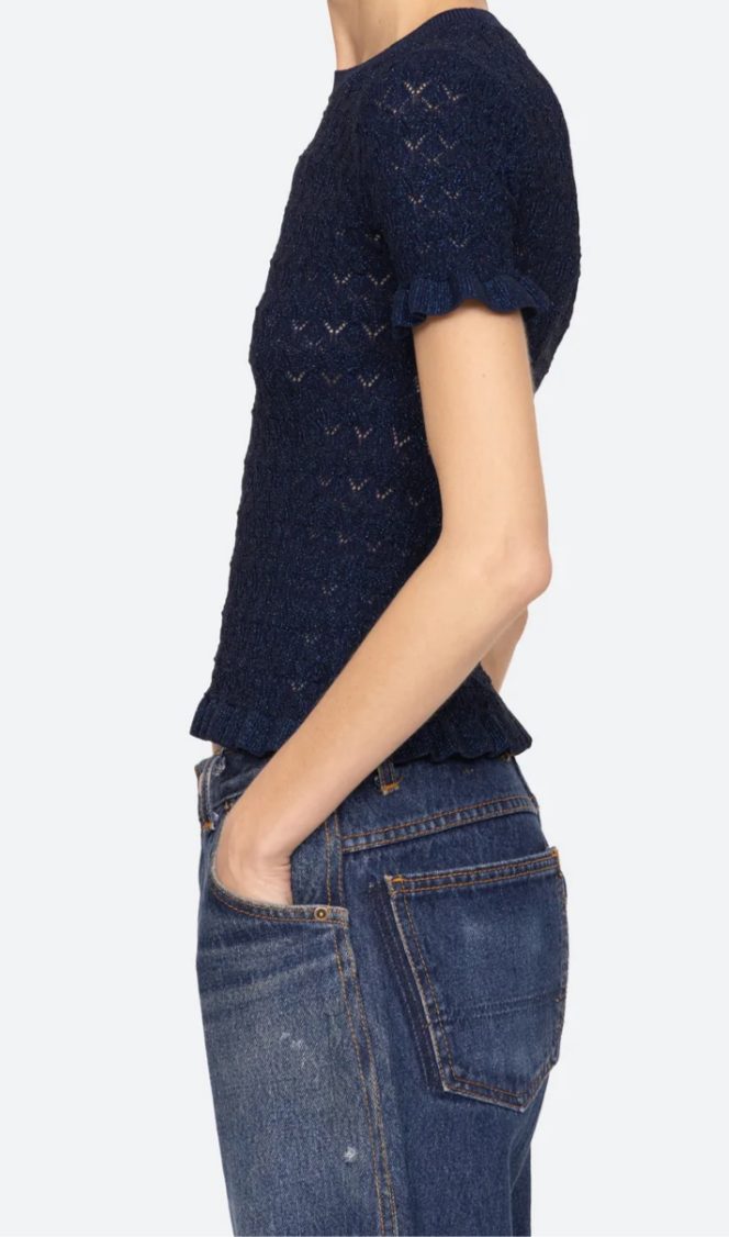 Woman wearing a navy blue knitted top and jeans on a white background