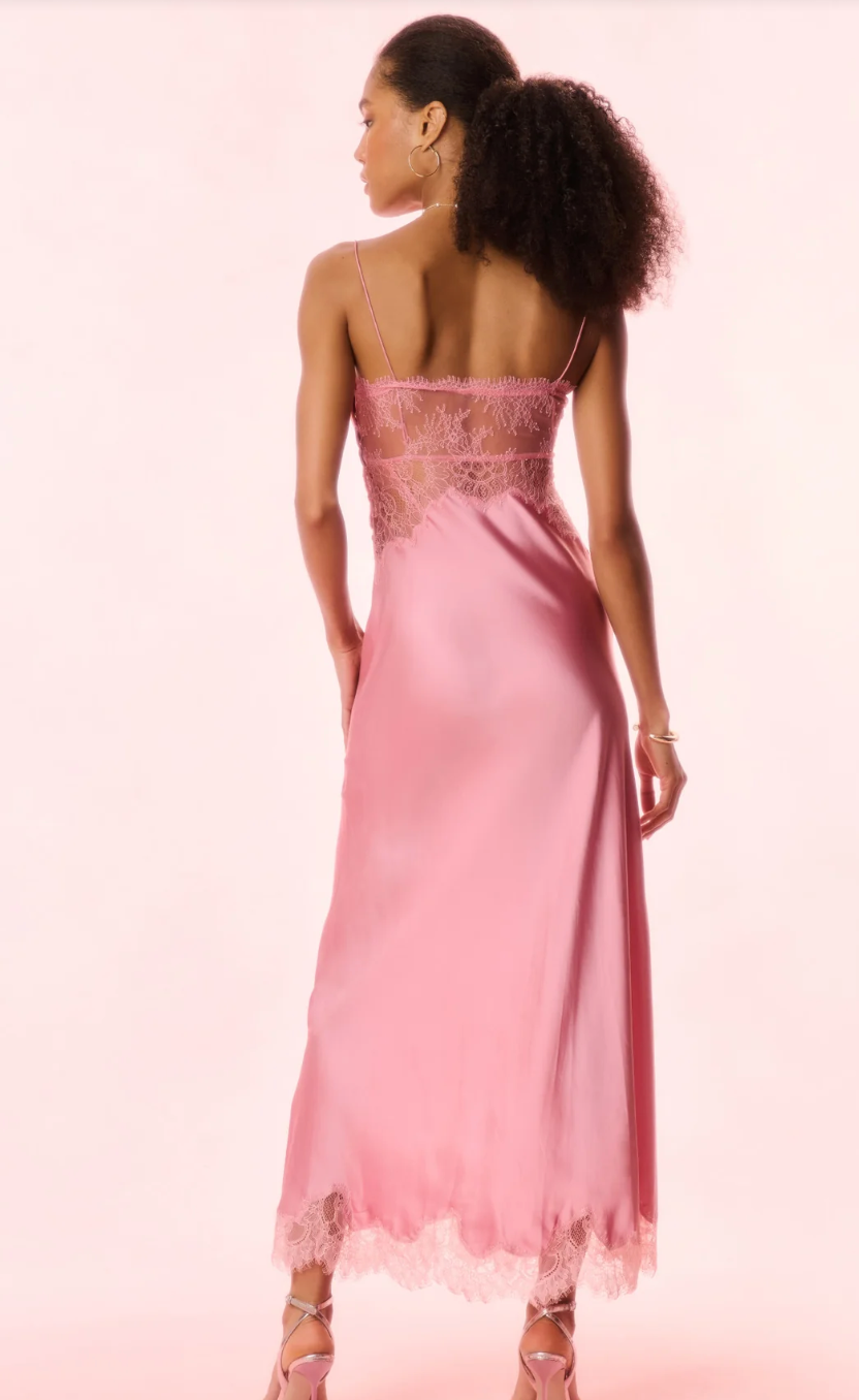 Woman wearing a pink evening gown with lace details on a light pink background