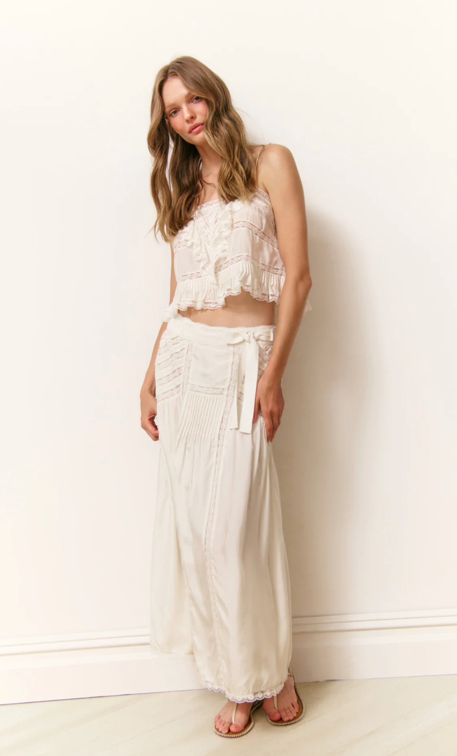 Woman wearing a white lace top and skirt against a white wall