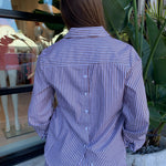 Person wearing a brown and white striped shirt with plants and a window in the background