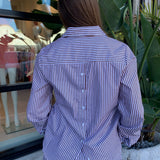 Person wearing a brown and white striped shirt with plants and a window in the background