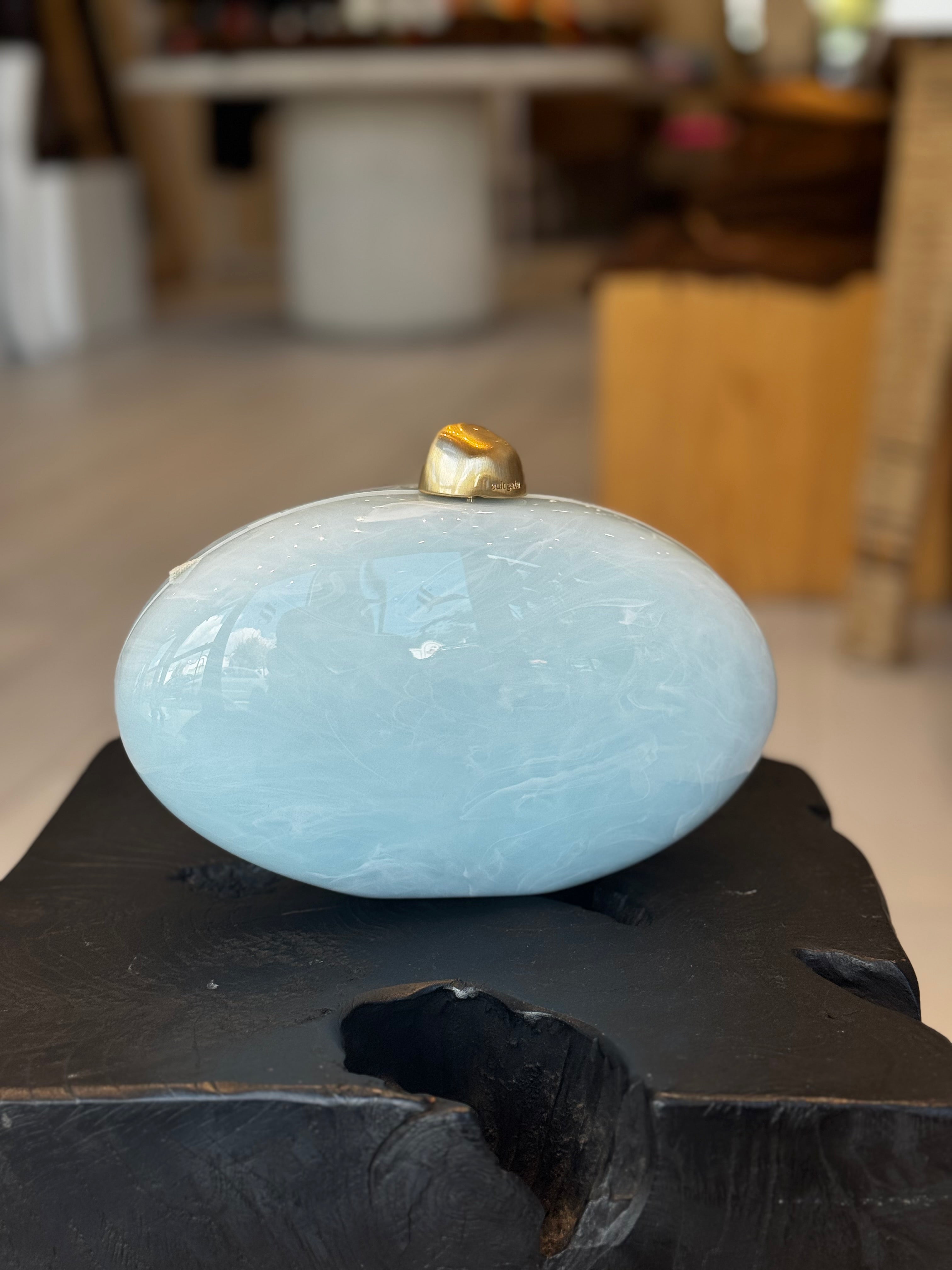 Light blue ceramic clutch with gold clasp on top on a dark surface, blurred indoor background