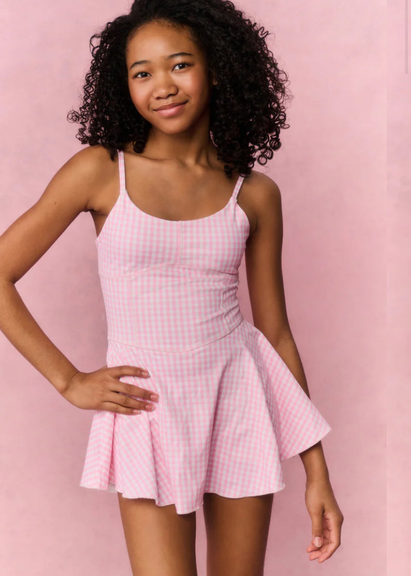 Young girl wearing a pink checkered dress against a pink background