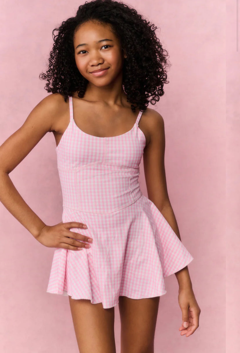 Young girl wearing a pink checkered dress against a pink background