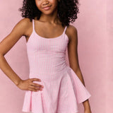 Young girl wearing a pink checkered dress against a pink background