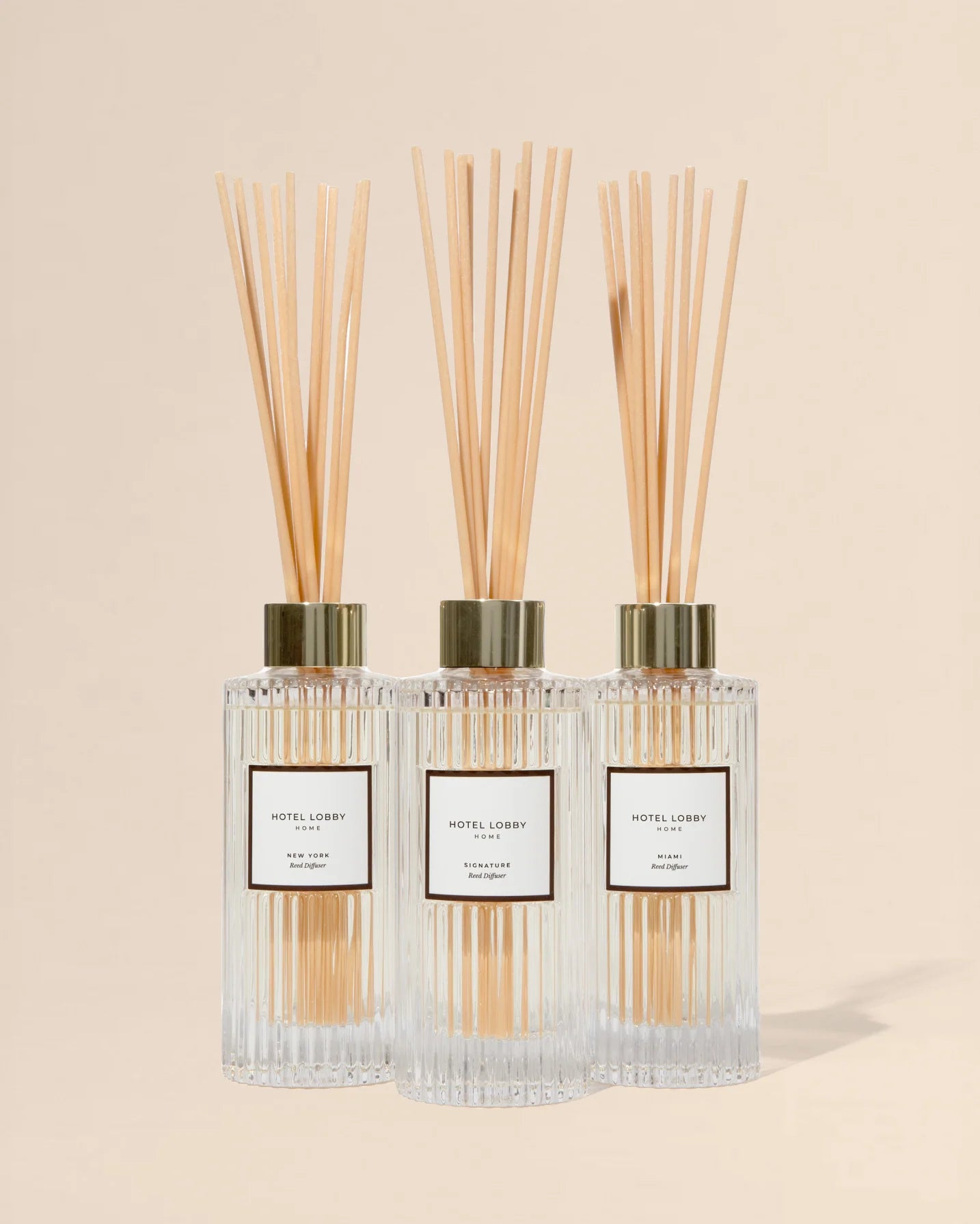 Three diffuser bottles with reeds on a beige background