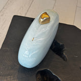 Light blue clutch with gold clasp on top sitting on a black wooded stool