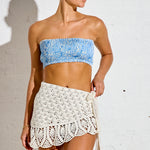 Woman wearing a blue bandeau top and white crochet skirt against a white background