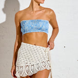 Woman wearing a blue bandeau top and white crochet skirt against a white background