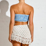 Woman wearing a blue strapless top and white crochet skirt against a white background