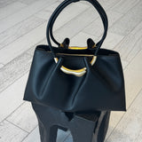 Black handbag with gold accents on a light wooden floor