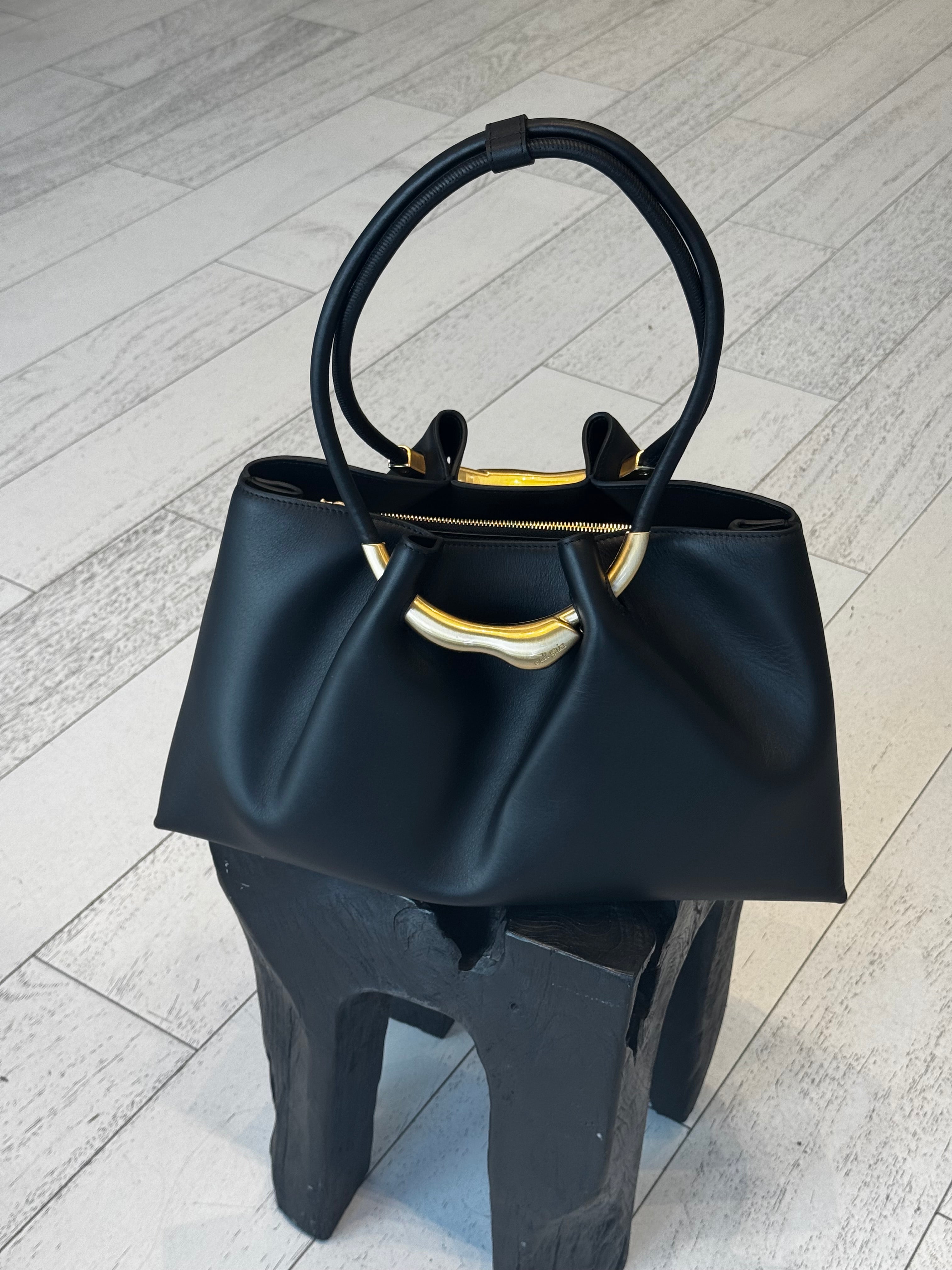 Black handbag with gold accents on a light wooden floor