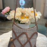 Textured handbag with brown straps on a marble surface with flowers in the background