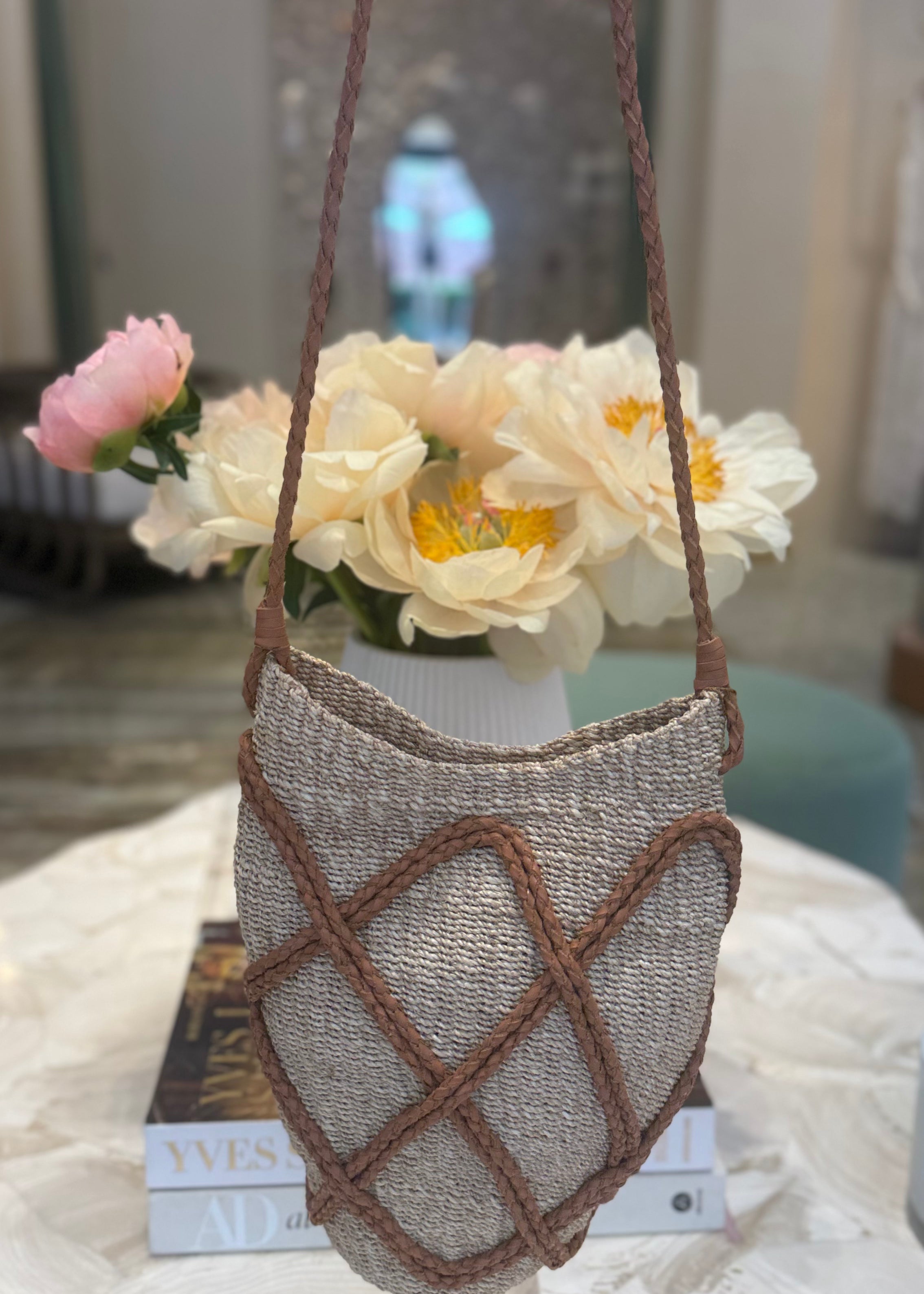 Textured handbag with brown straps on a marble surface with flowers in the background