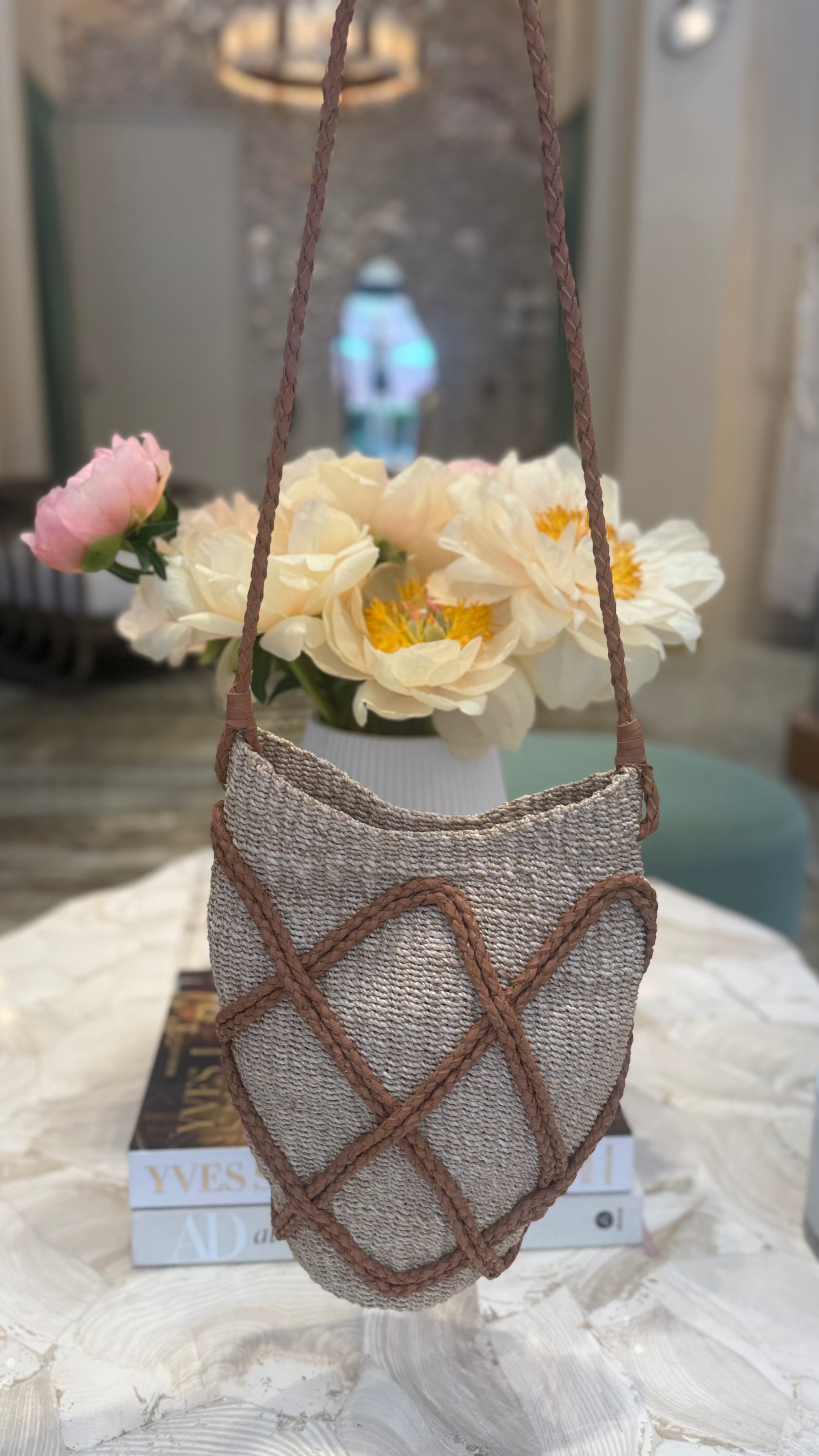 Textured handbag with brown straps on a marble surface with flowers in the background