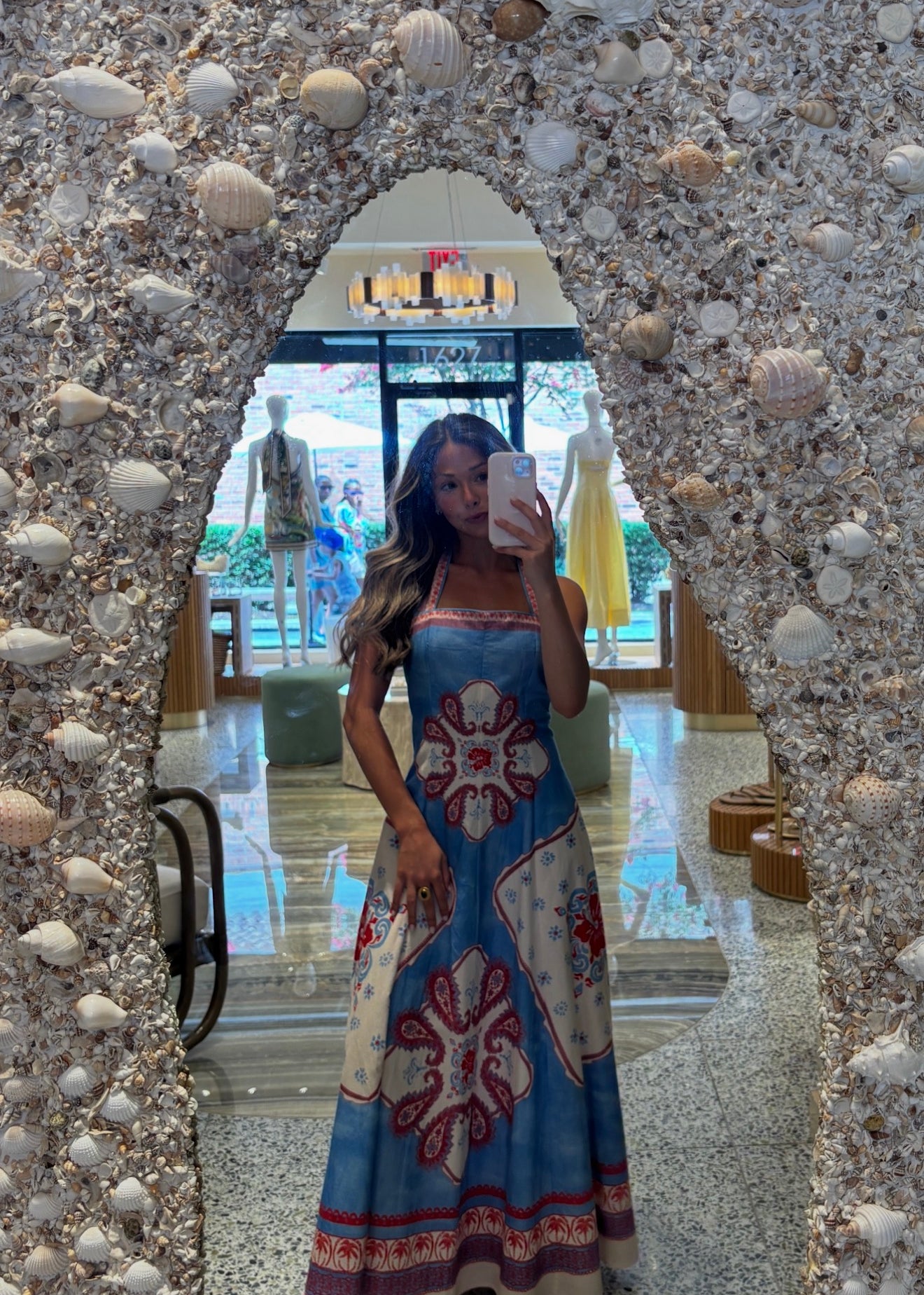 Woman taking a mirror selfie wearing a colorful dress in front of a textured wall.