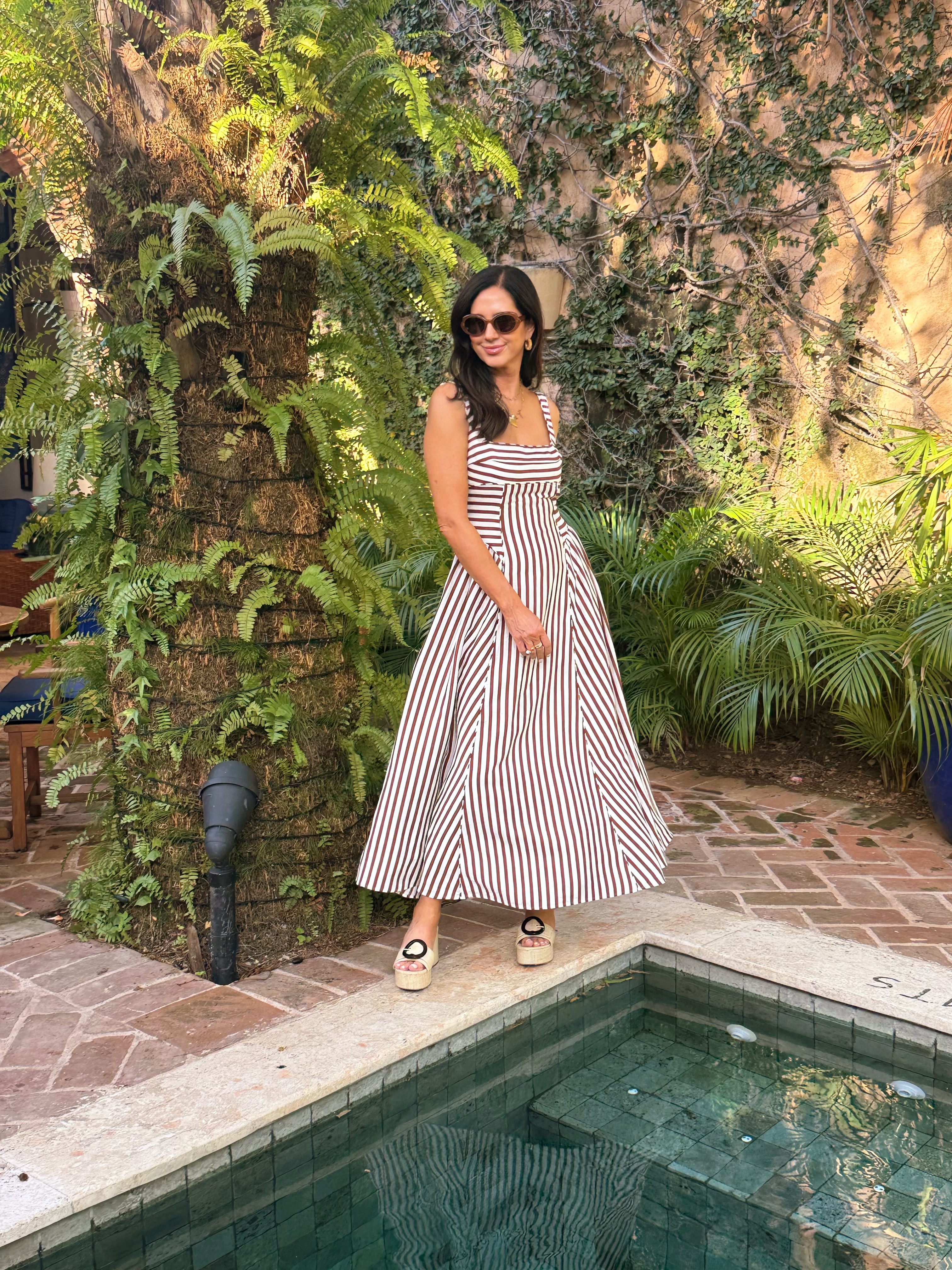 Woman in a striped dress standing by a pool with greenery around
