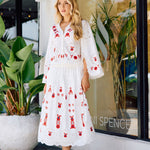 Woman in a white dress with red embroidery standing in front of a store window.