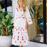 Woman in a white dress with red embroidery standing in front of a store window.