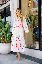 Woman in a white dress with red embroidery standing in front of a store window.