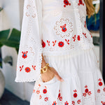 White skirt and top with red floral embroidery worn by a person.