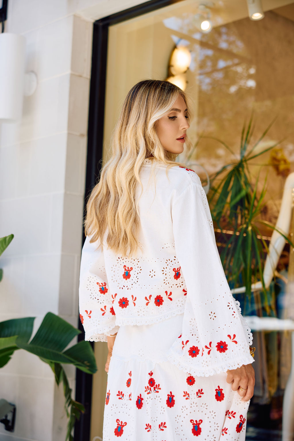 Woman wearing a white skirt and top with red floral embroidery standing indoors.