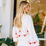 Woman wearing a white skirt and top with red floral embroidery standing indoors.