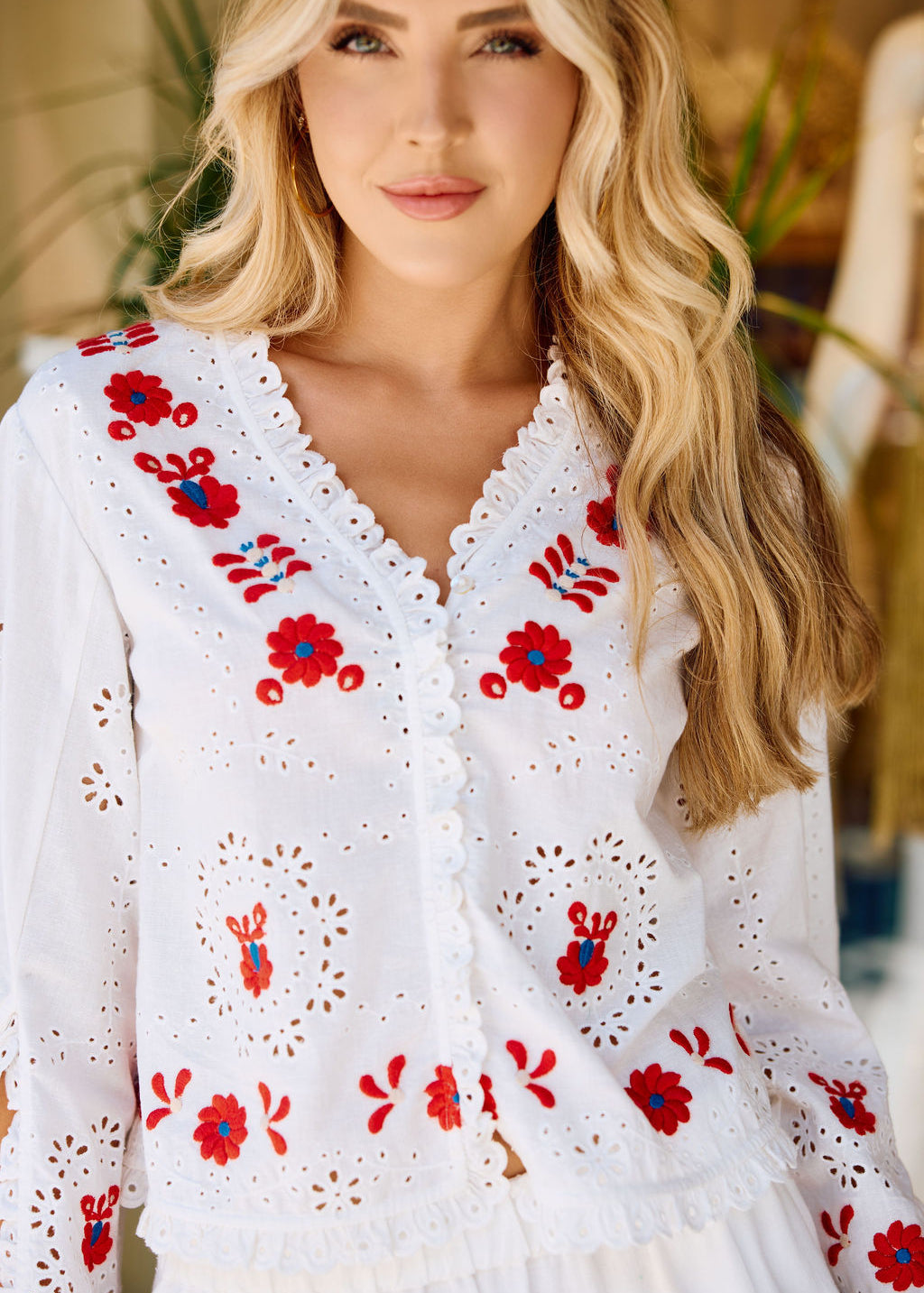 Woman wearing a white blouse with red floral embroidery in an indoor setting.
