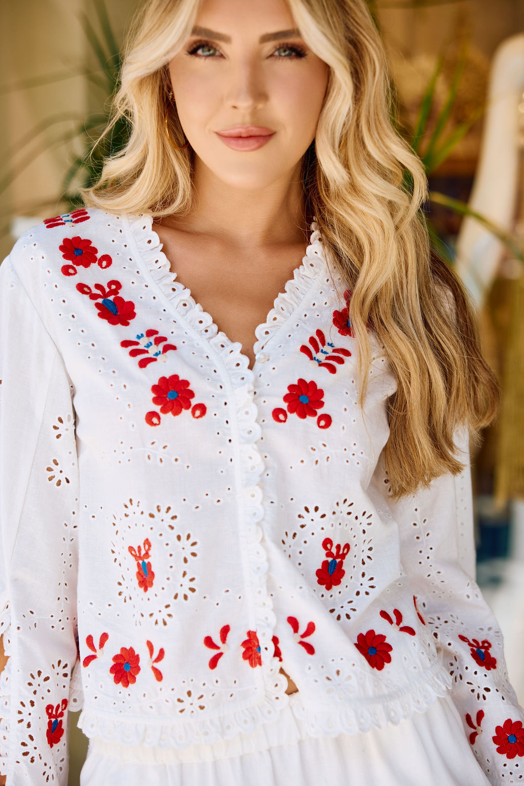 Woman wearing a white blouse with red floral embroidery in an indoor setting.