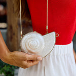 Person holding a white with gold accenting shell-shaped handbag with a red top and white skirt.