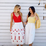 Two women standing on a wooden deck, wearing colorful sets against a white wall.