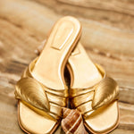 Gold sandal with shell design on a wooden surface