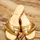 Gold sandal with shell design on a wooden surface