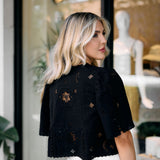 Woman wearing a black embroidered top in front of a store window