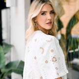 Woman wearing a white lace top with floral patterns in an outdoor setting.