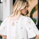 Woman wearing a white blouse with floral embroidery in an outdoor setting