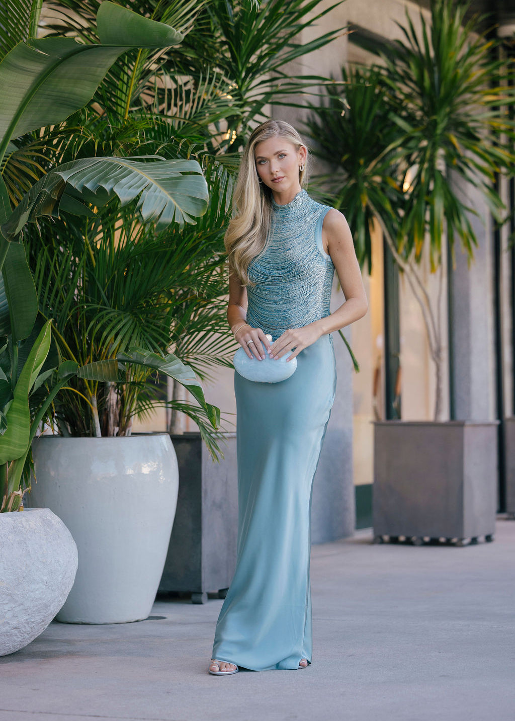 Woman in a light blue dress standing among potted plants