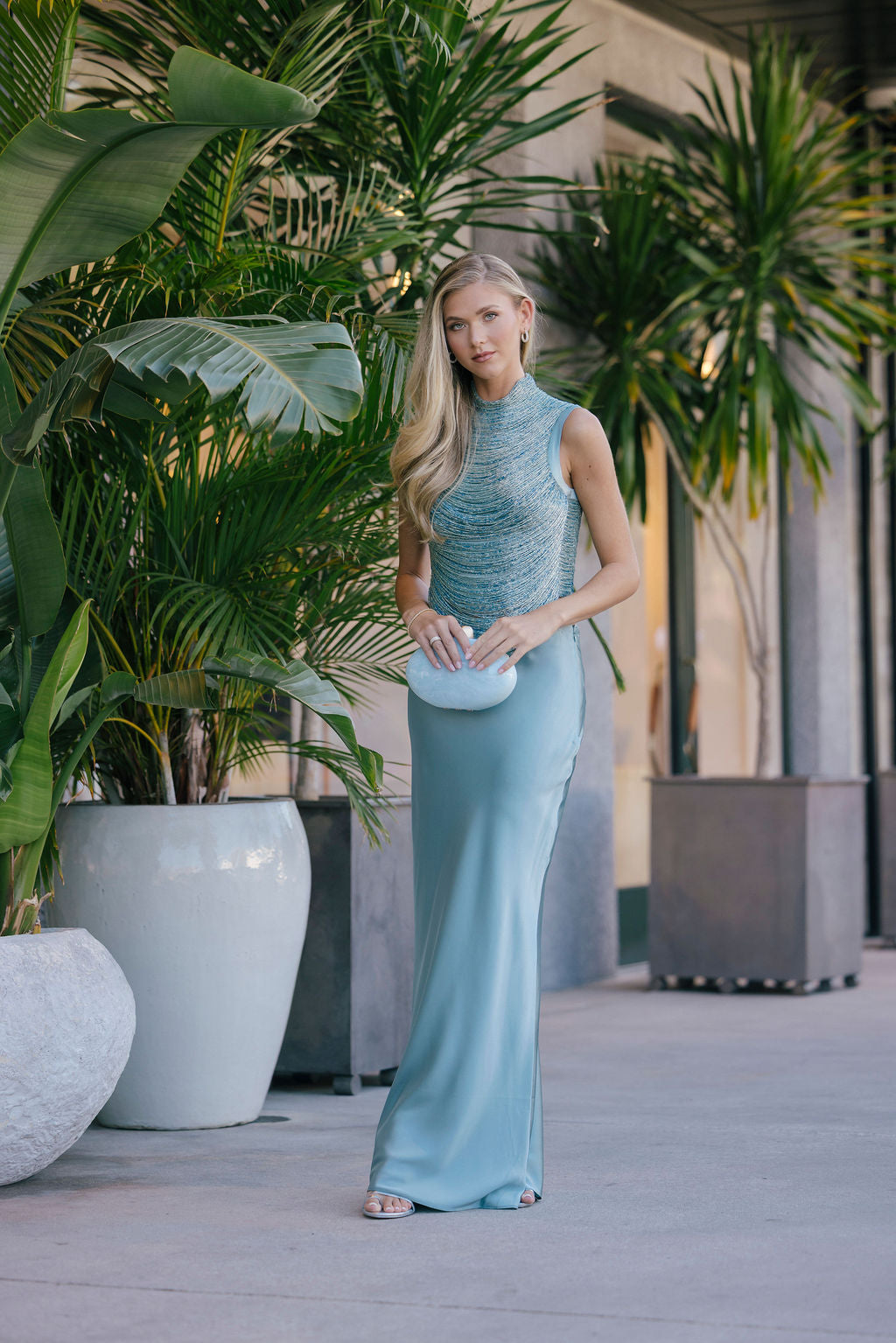 Woman in a light blue dress standing among potted plants