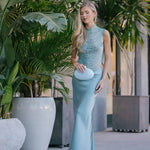 Woman in a light blue Beaded top and long skirt standing among potted plants