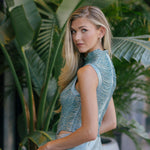 Woman in a blue top and light blue pants standing among green plants