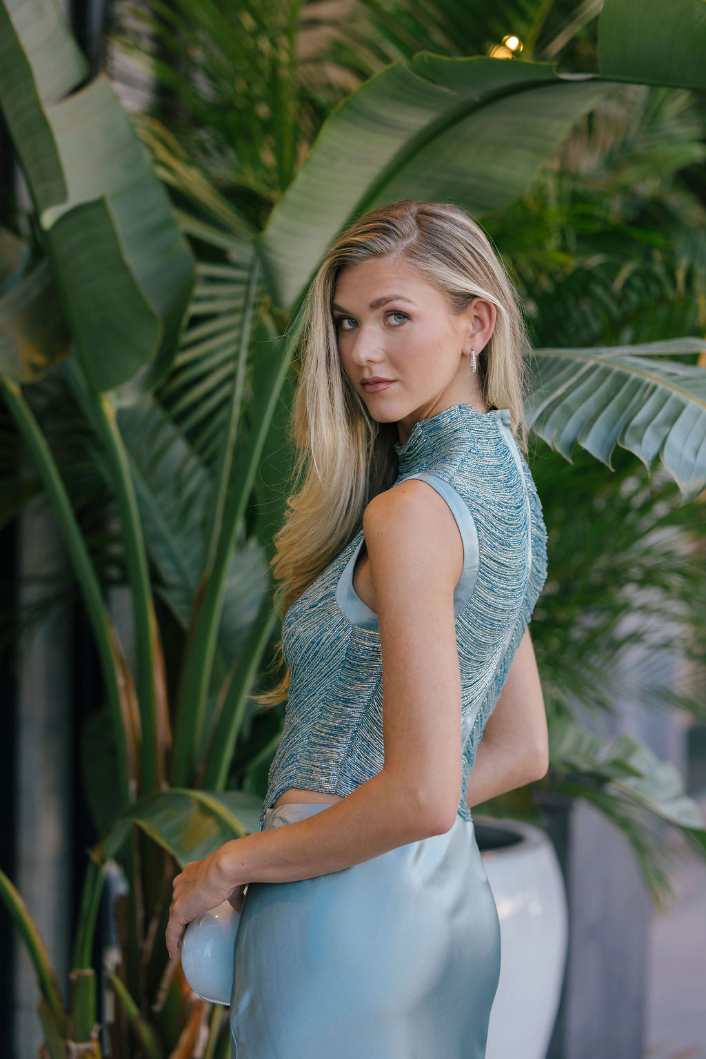 Woman in a blue top and light blue pants standing among green plants