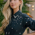Woman wearing a black dress with silver embellishments in an outdoor setting.