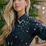 Woman wearing a black dress with silver embellishments in an outdoor setting.