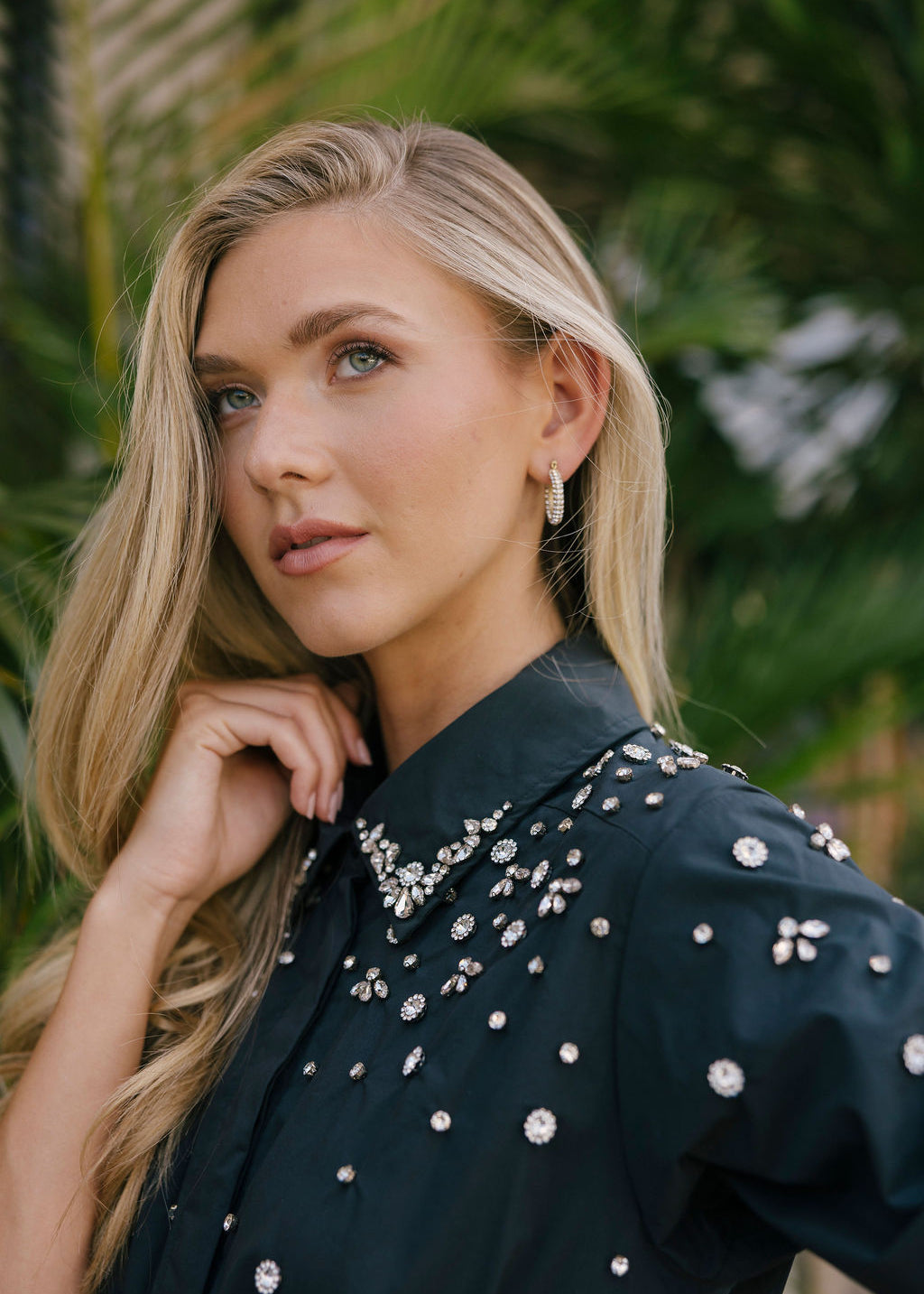 Woman wearing a black dress with silver embellishments against a green leafy background