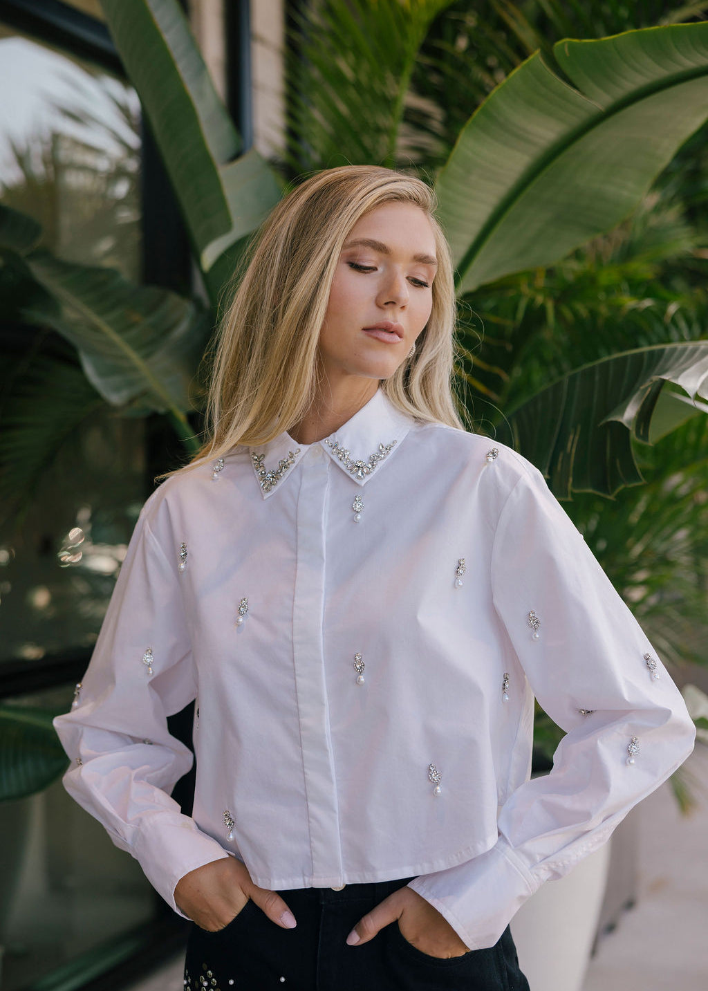 Woman wearing a white embellished shirt with green foliage in the background