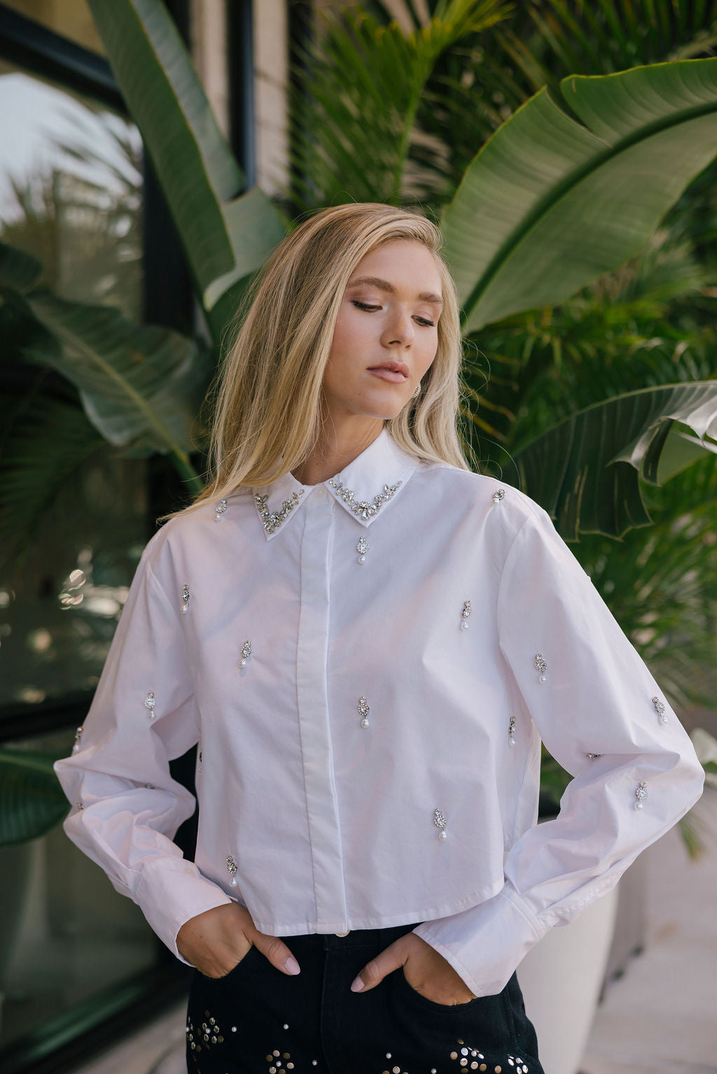 Woman wearing a white embellished shirt with green foliage in the background